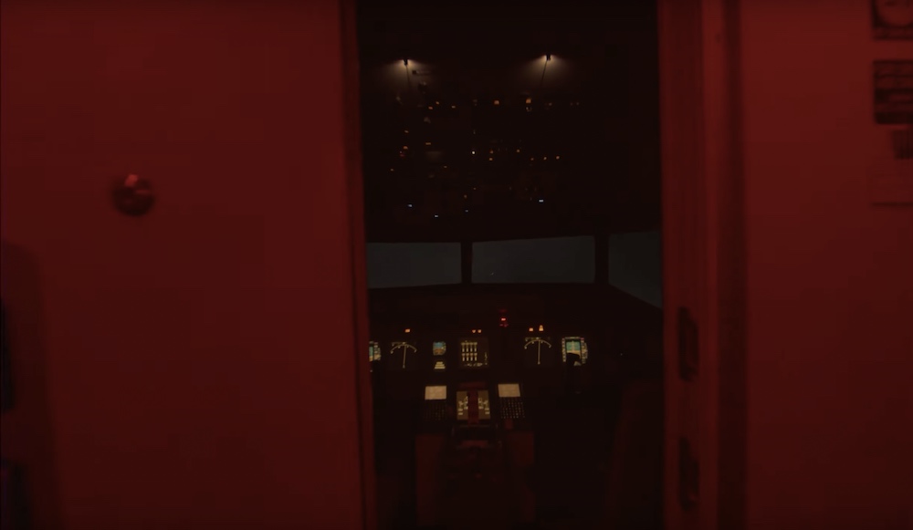 View into the cockpit of an airliner. The space is lit dimly red.