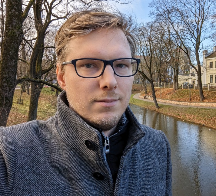 man with blond hair and short blond beard with glasses in front of a river