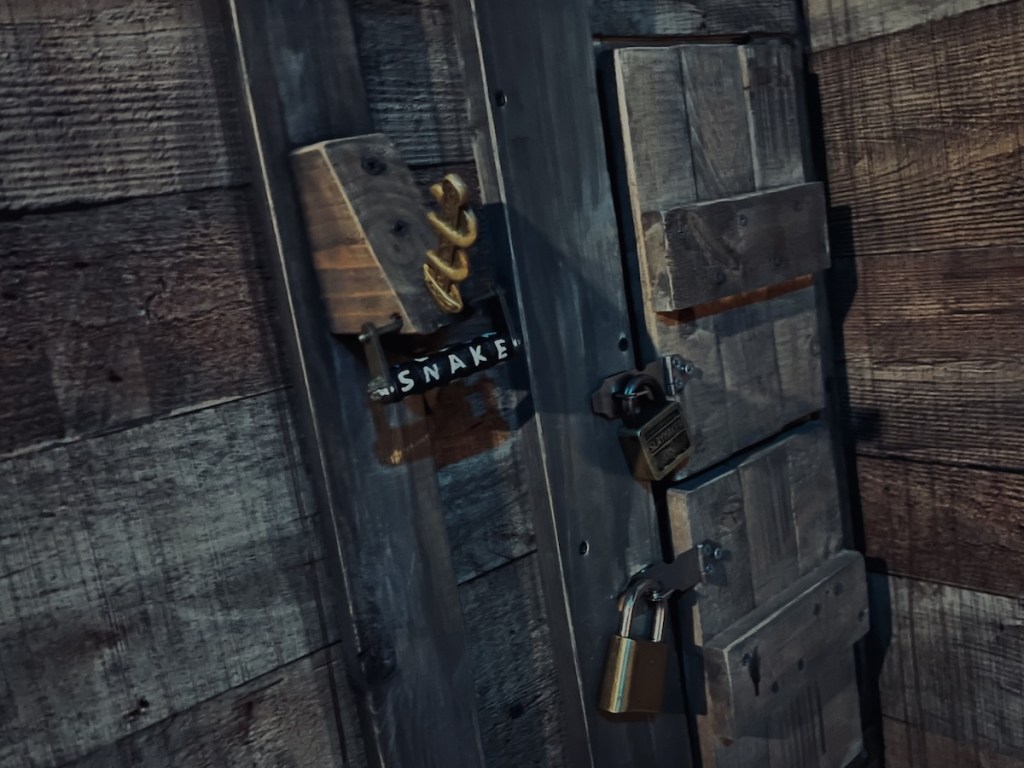 A wooden wall with 3 locked compartments. One has a letter lock that reads, "SNAKE"