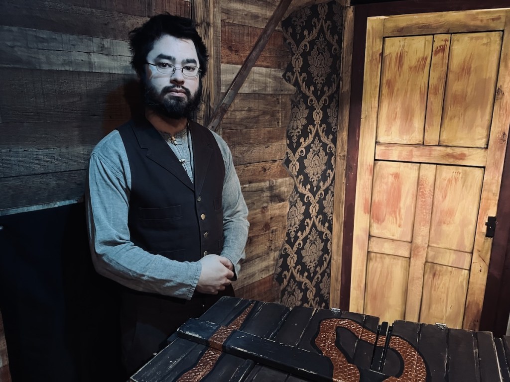 A pale, well-dressed man in dated clothes in an old attic.