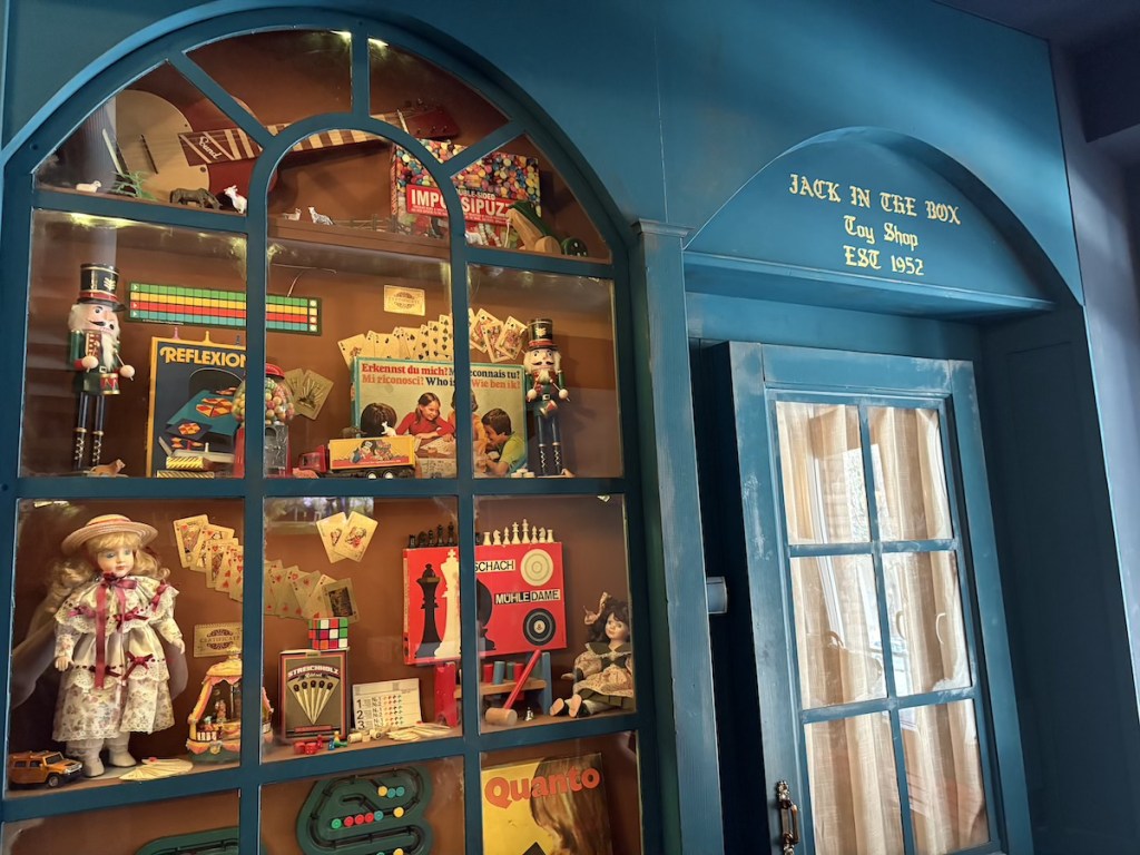 The front facade of an old toy shop. The front window is filled with classic kids toys. The signage reads, "Jack in the Box Toy Shop EST 1952"
