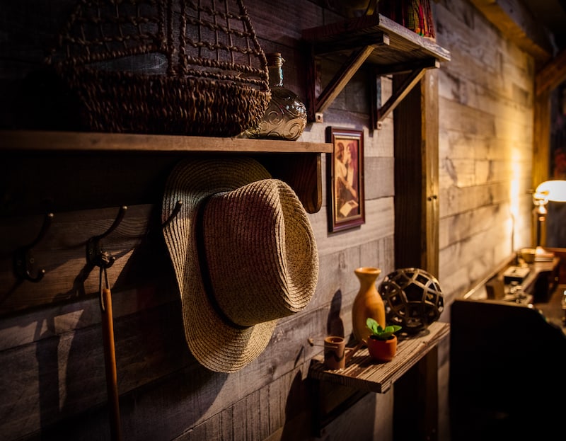 In-game: the wooden wall of a cabin with small shalves and hooks displaying many different trinkets.