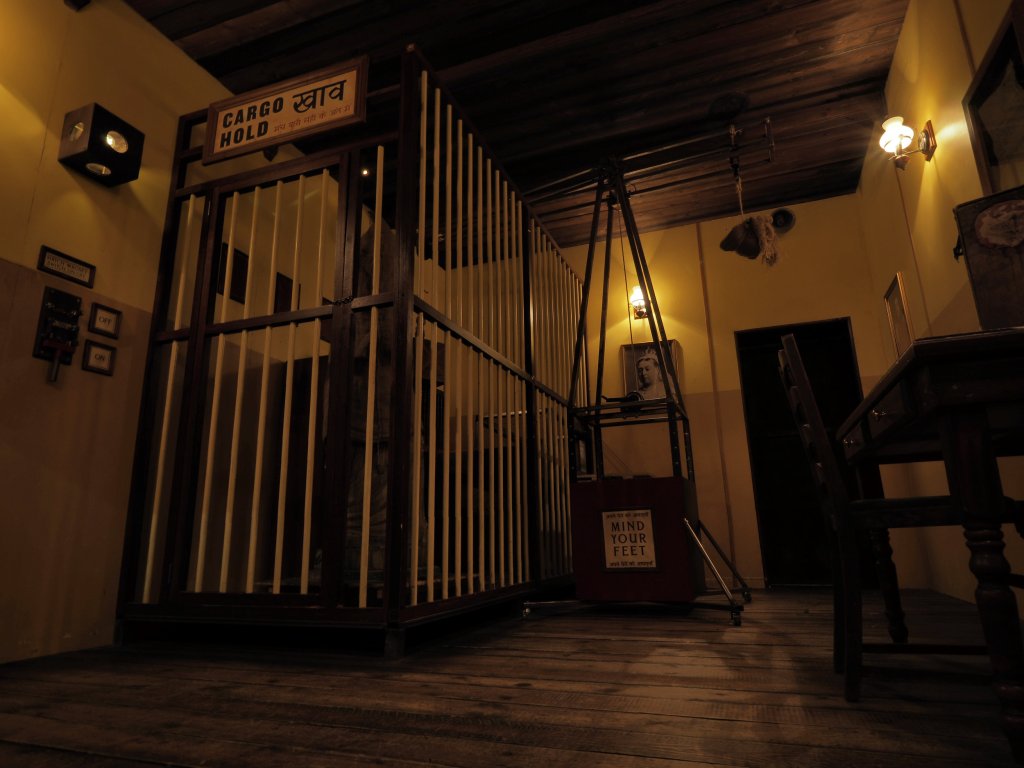 dim room with yellow walls. there is a large cage on one side and table on the other.