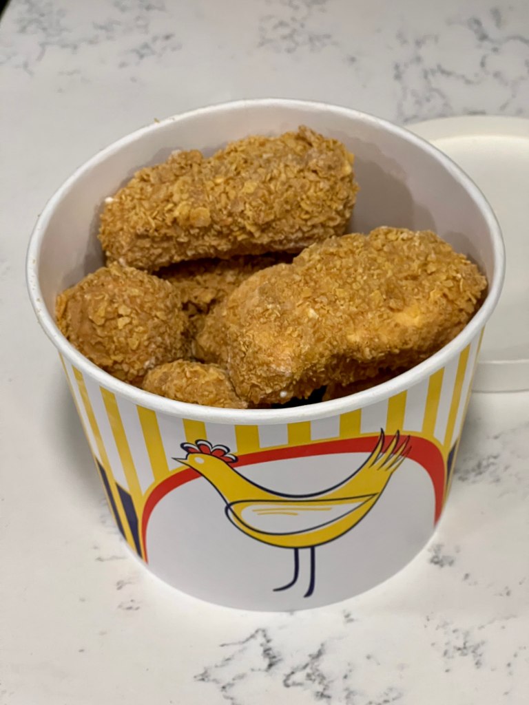 a paper bucket with an image of a chicken on it containing ice cream dipped in cornflakes resembling fried chicken