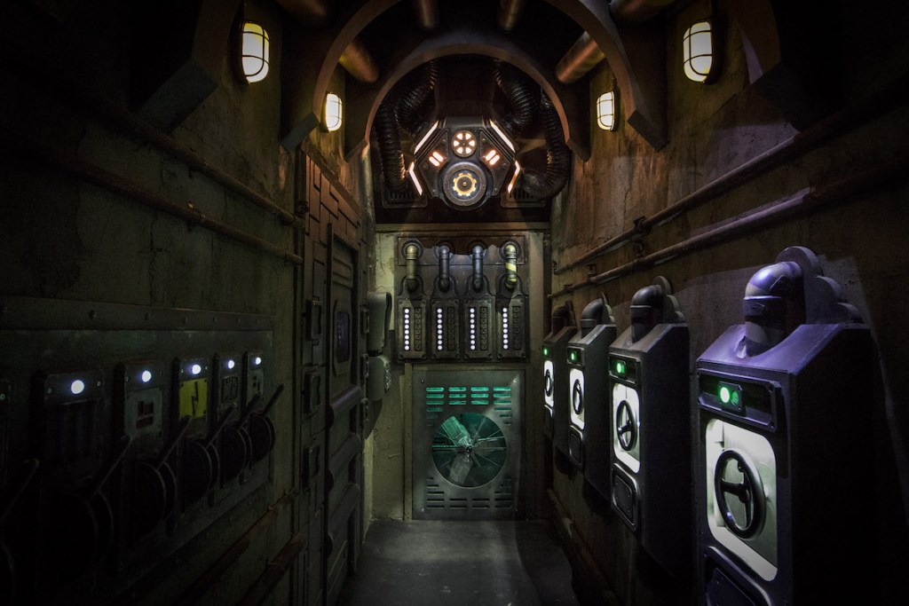 A long corridor that looks like a cross between a sewer and a machine with various wheels and switches.