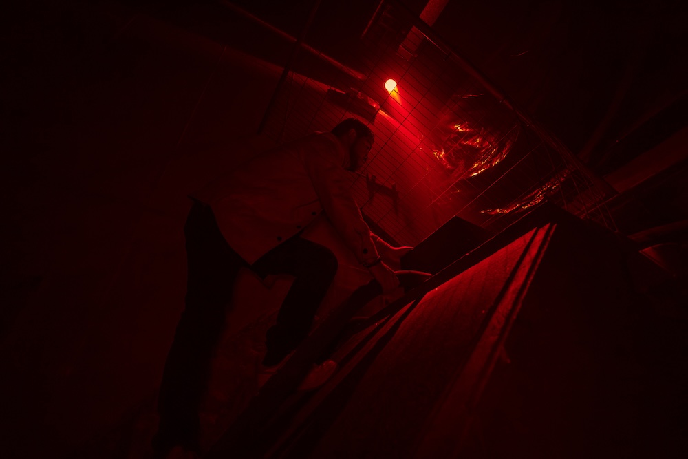 A person leans over, opening a hatch while bathed in red light.