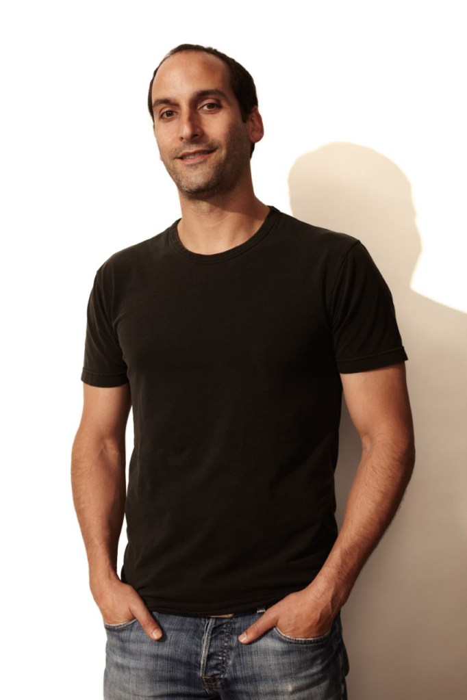 Man in black t-shirt and jeans with short hair and slight grin
