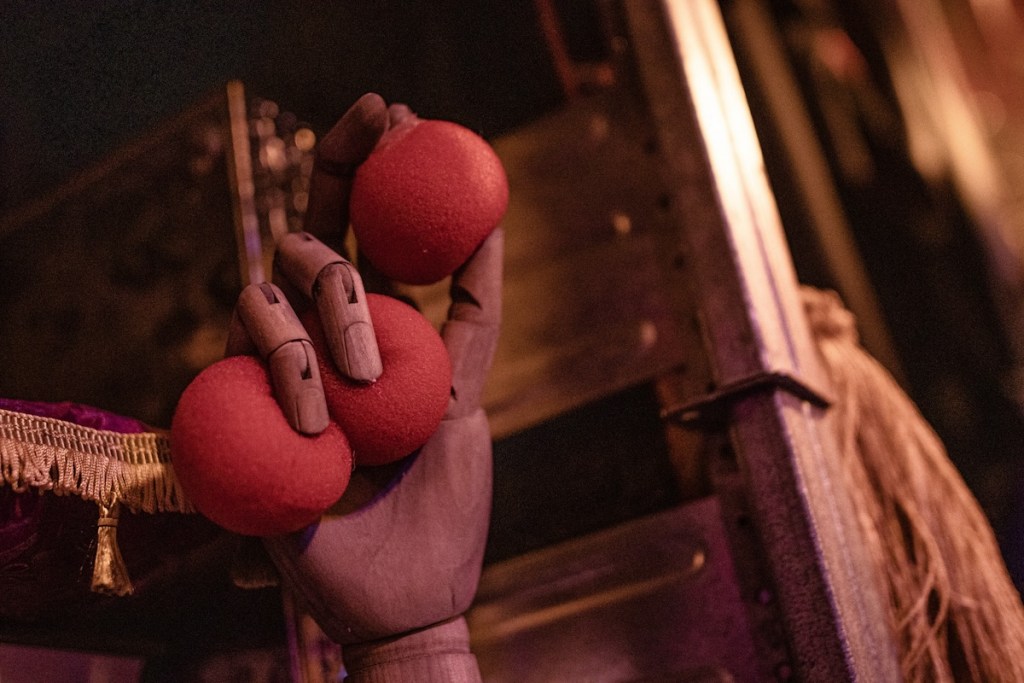 a wooden hand holding three soft red balls