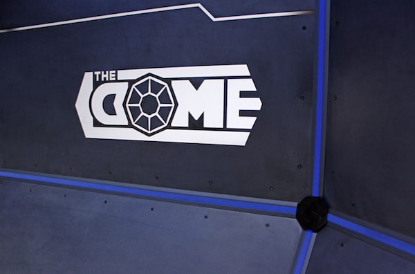In-game: The Dome's logo glowing on a steel wall.