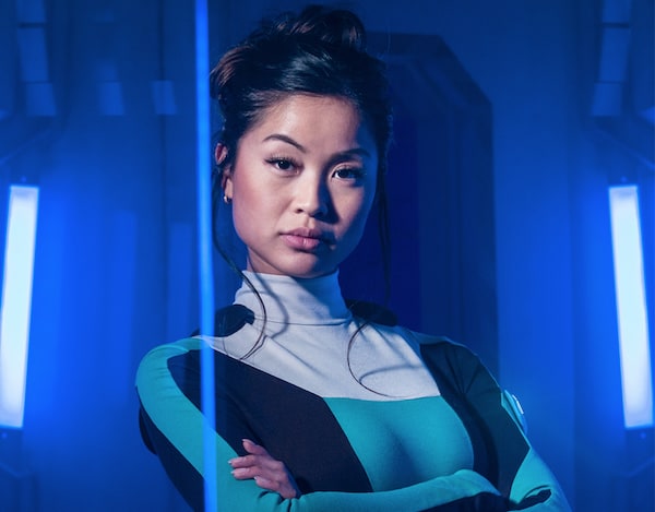 A beautiful woman in a tight body suit, arms crossed, looking into the camera.