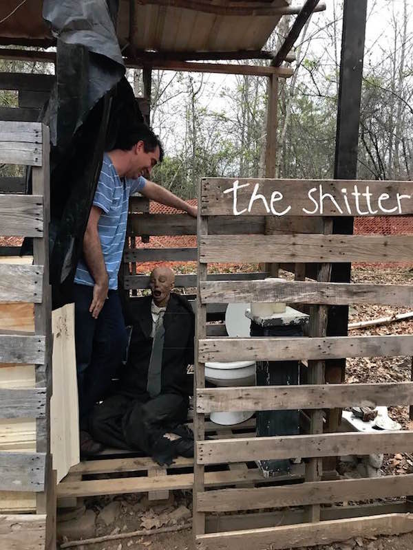 Dan Egnor standing in an outhouse labeled "The Shitter" looking into the toilet.