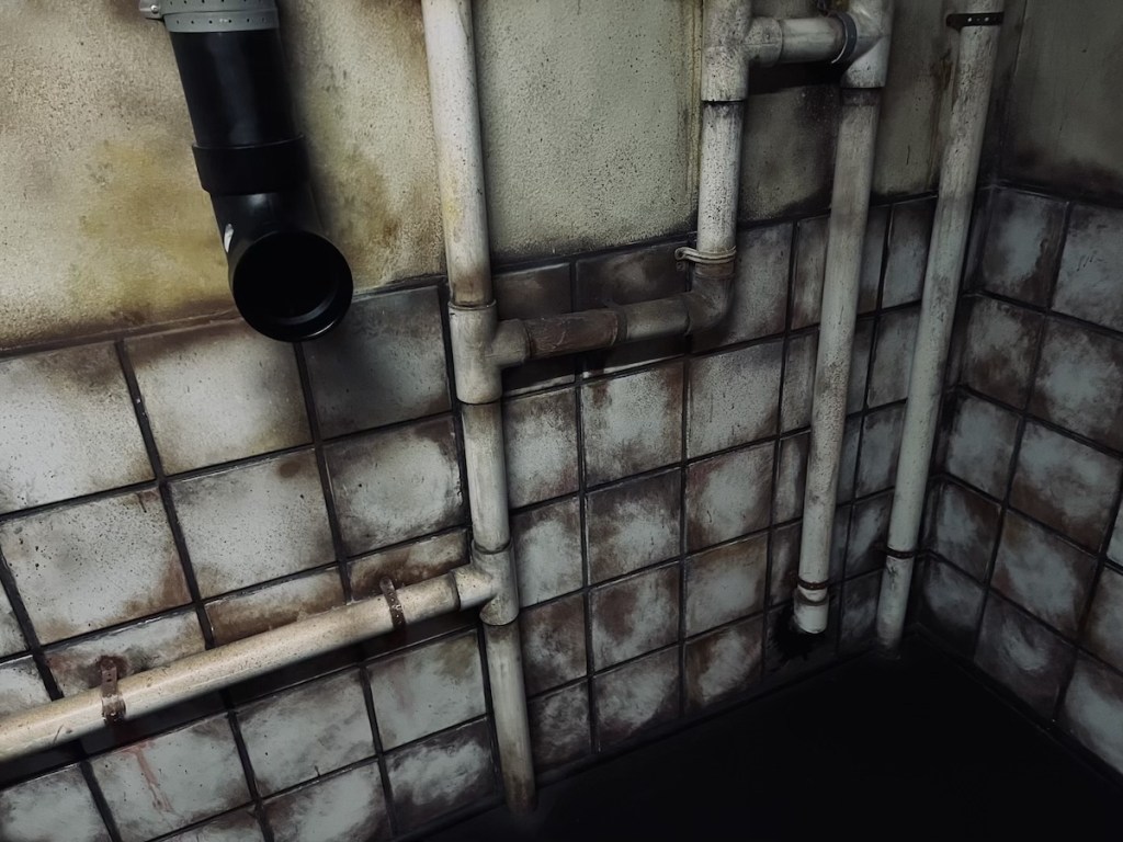 SAW-like escape room with dingy tiles and PVC pipes running against the wall.