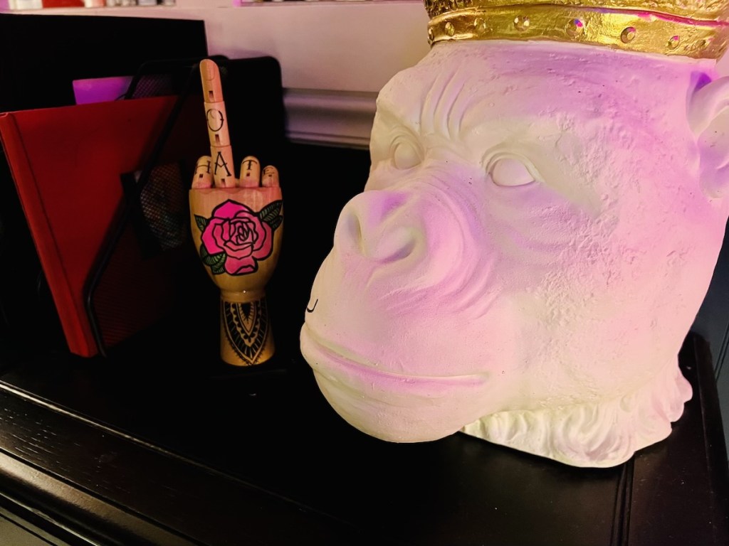 A sculpture of a gorilla wearing a crown beside a wooden hand covered in tattoos raising its middle finger.