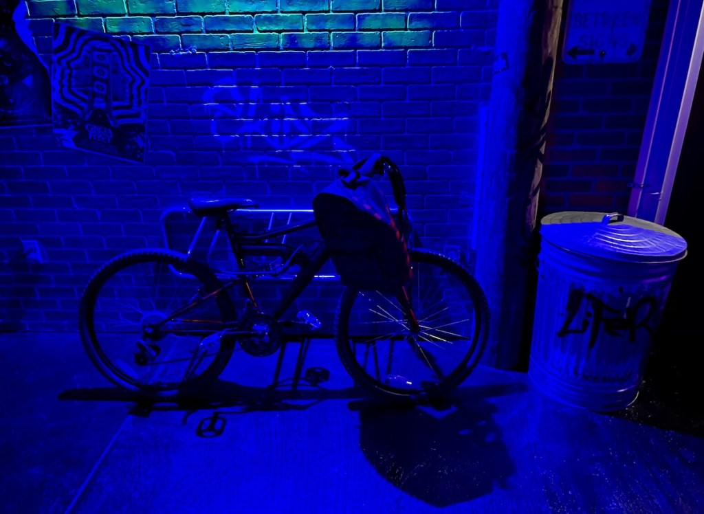 A bicycle with a backpack locked to a rack in a graphited alley.