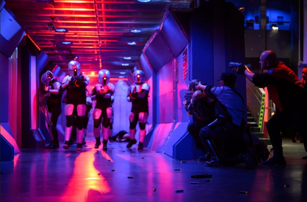Alien invaders in armor walking down colorfully lit space station hallway, with fighters waiting around the corner with weapons