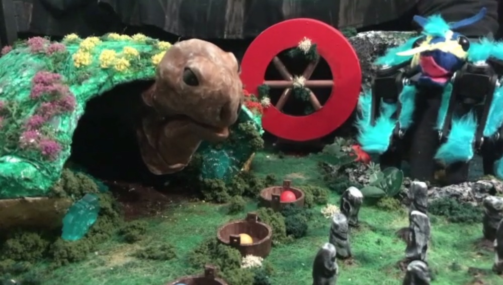 A large turtle puppet in a diorama beside a bule spider puppet.