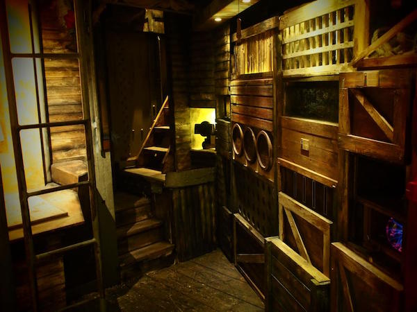 In-game: A wooden ship's comaptment with unusual crates and storage containers built into the walls.