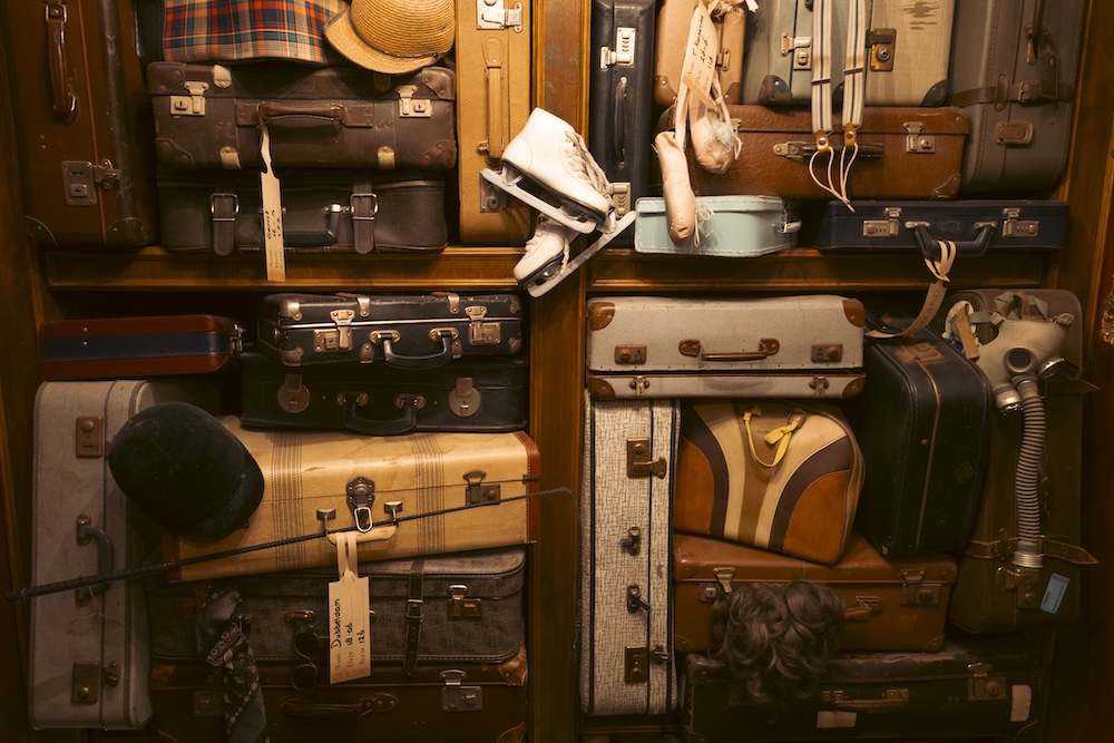 A wall filled with luggage, and personal items including ice skates, hats, and a gas mask.