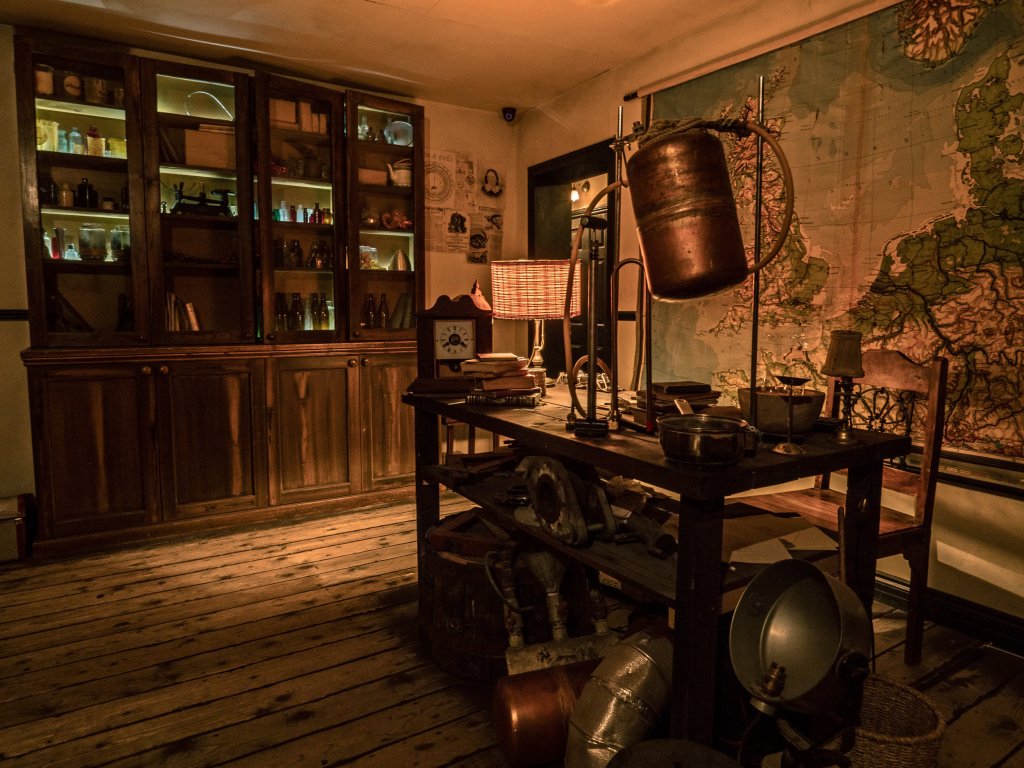 old timey looking room with a large map on the wall, bookcases and a table with scientific instruments