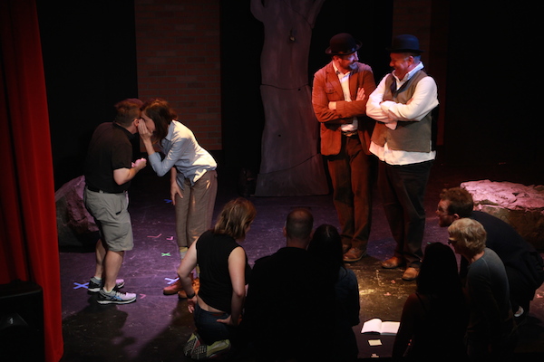 Two actors standing on stage while another actor whispers to a player