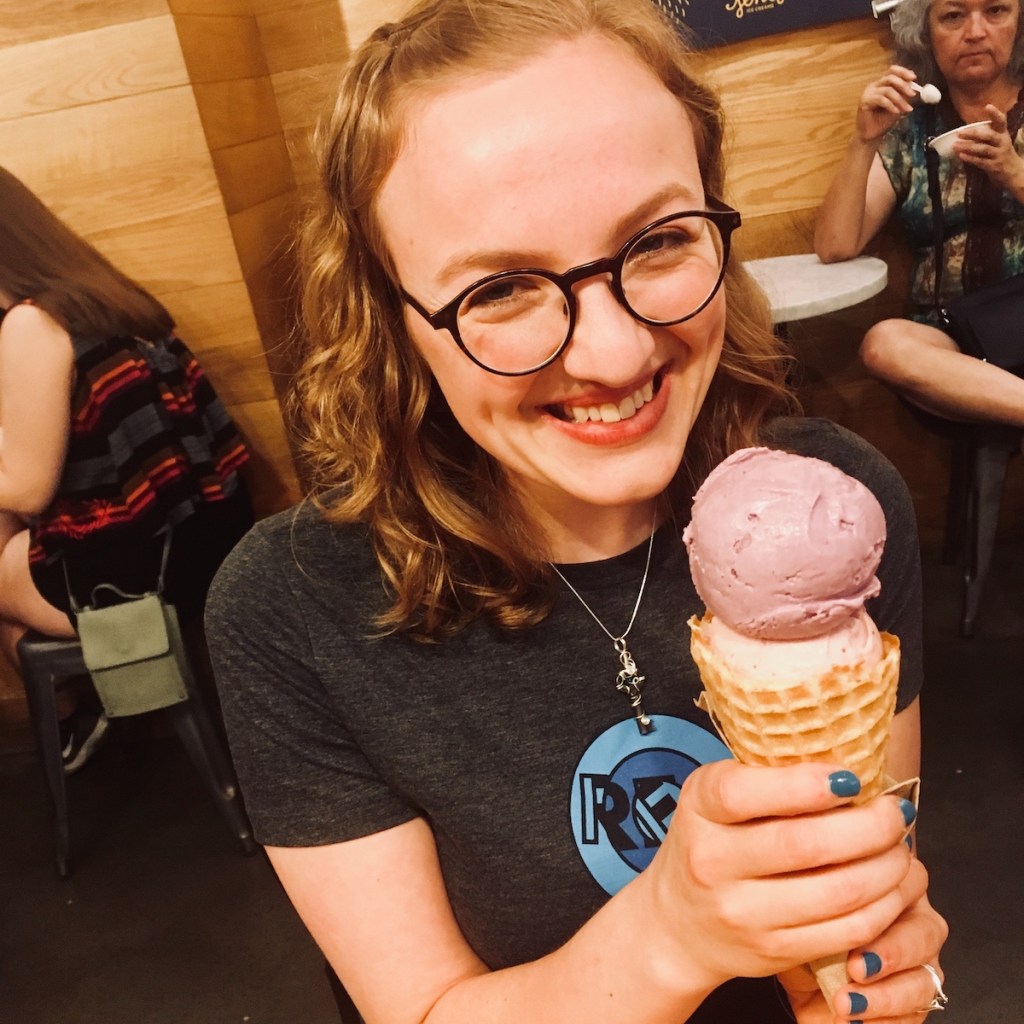 Lisa in a REA shirt holding a large ice cream cone in her hand, she has an eager look on her face.