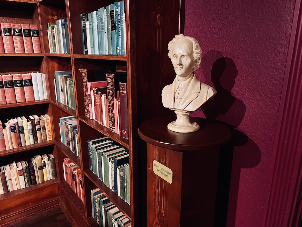 Bookshelves filled with books beside a sculpture of Hans Christian Andersen.