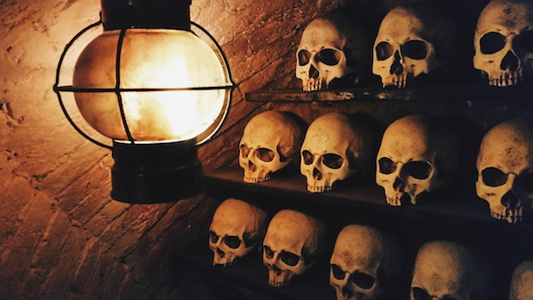 In-game: a wall of human skulls lit by a lantern.