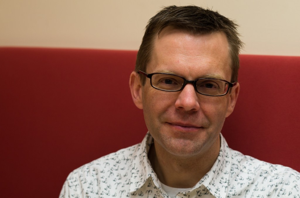 caucasian man with glasses and short hair wearing a patterned, white button down shirt