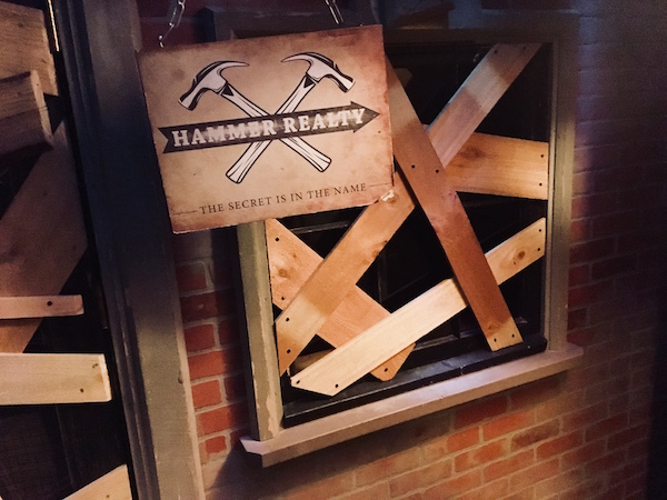 In-game: a boarded up business with a sign out front that says, "Hammer Realty, the secret is in the name."