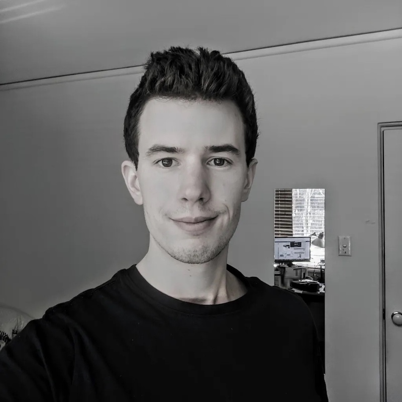 black and white photo of clean shaven man smiling with brown hair in a long sleeve black t-shirt