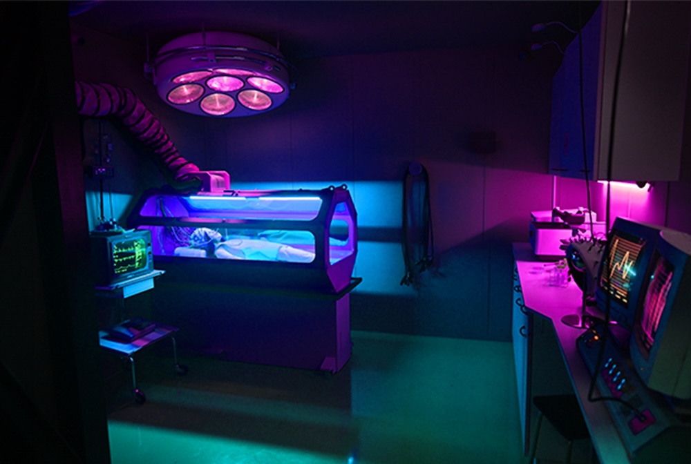A strange science lab with a body inside of a tube and covered in electronics.