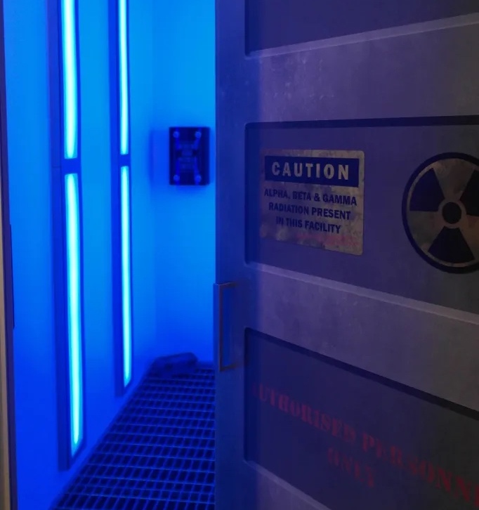 door opening into a blue lit room. door has a nuclear hazard caution sign.