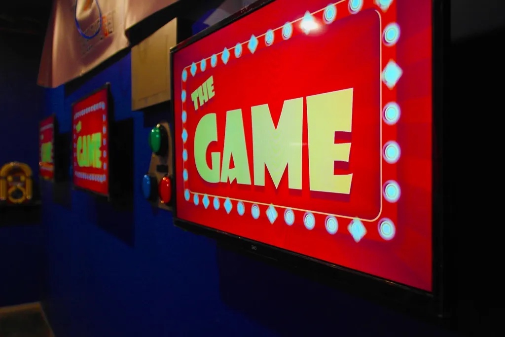 televisions with images that say "the game" surrounded by bright lights, against a blue wall.