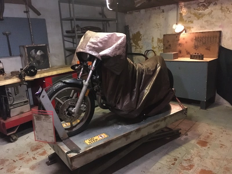In-game: An autoshop of a motorcycle in the middle covered with a tarp.