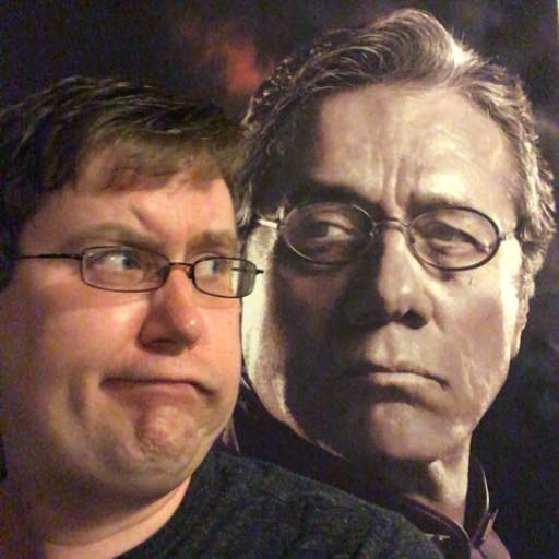 Image of man wearing glassess with short brown hair. He has a tight lipped grumpy expression, and he is looking slightly over his shoulder towards an image of Captain Adama from the TV show Battlestar Galactica. Adama is a middle aged man wearing glasses and a haughty expression.