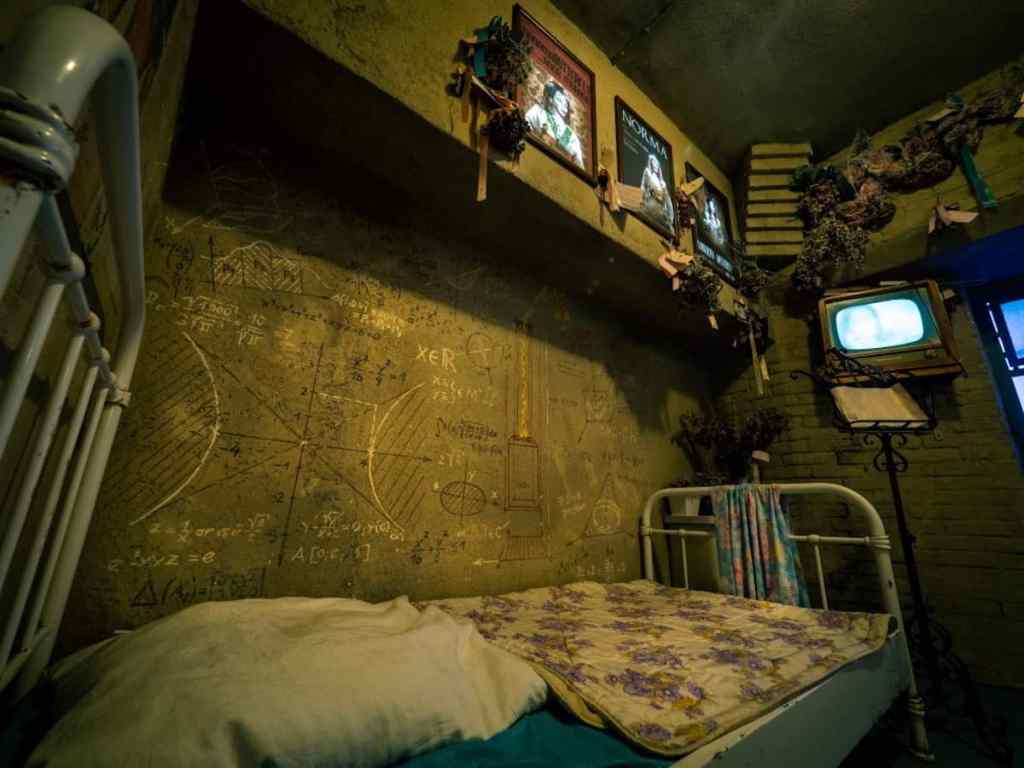 bed with metal frame in a dingy room with scribbles on the wall and photos above.