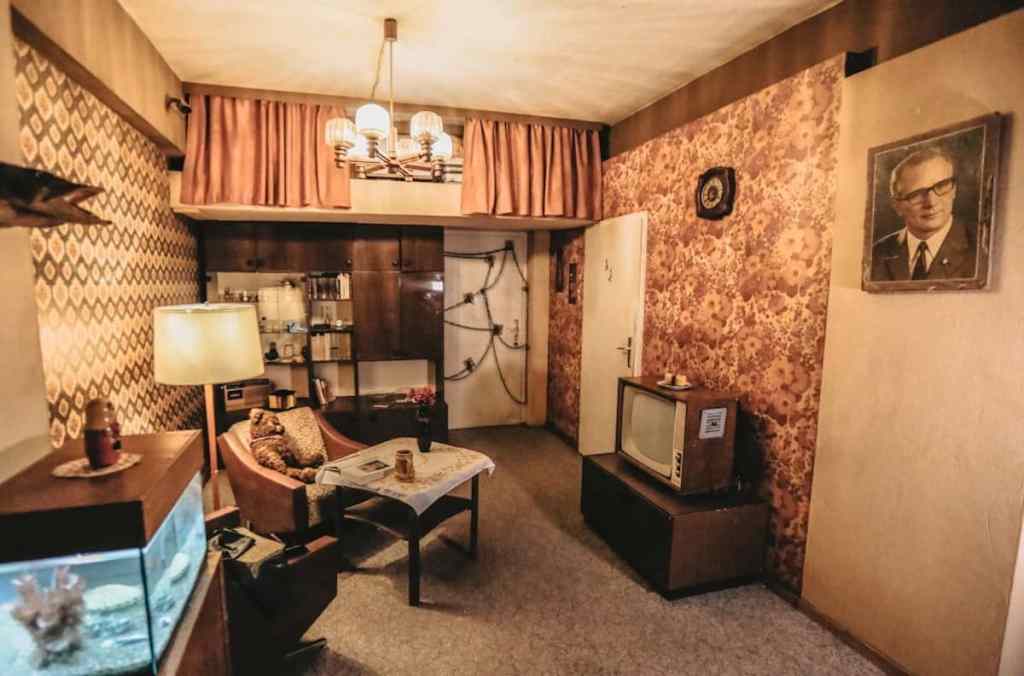 a living room from 80's east germany with an aquarium, tv, and chains and locks on a door.