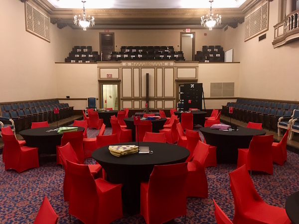 In-game: View of the room from the stage with 8 different tables, and a balcony full of seats above.
