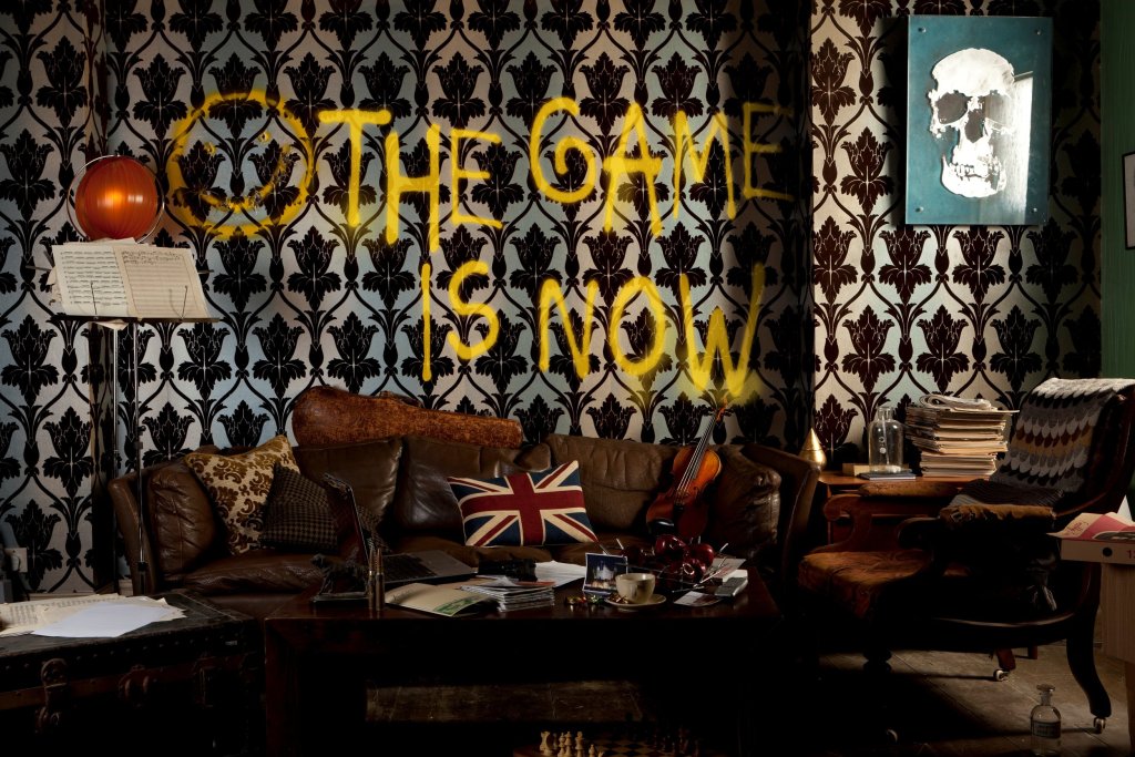 Living room decorated like it's from the 1060's. The words "the game is now" is spraypainted on the wallpaper.