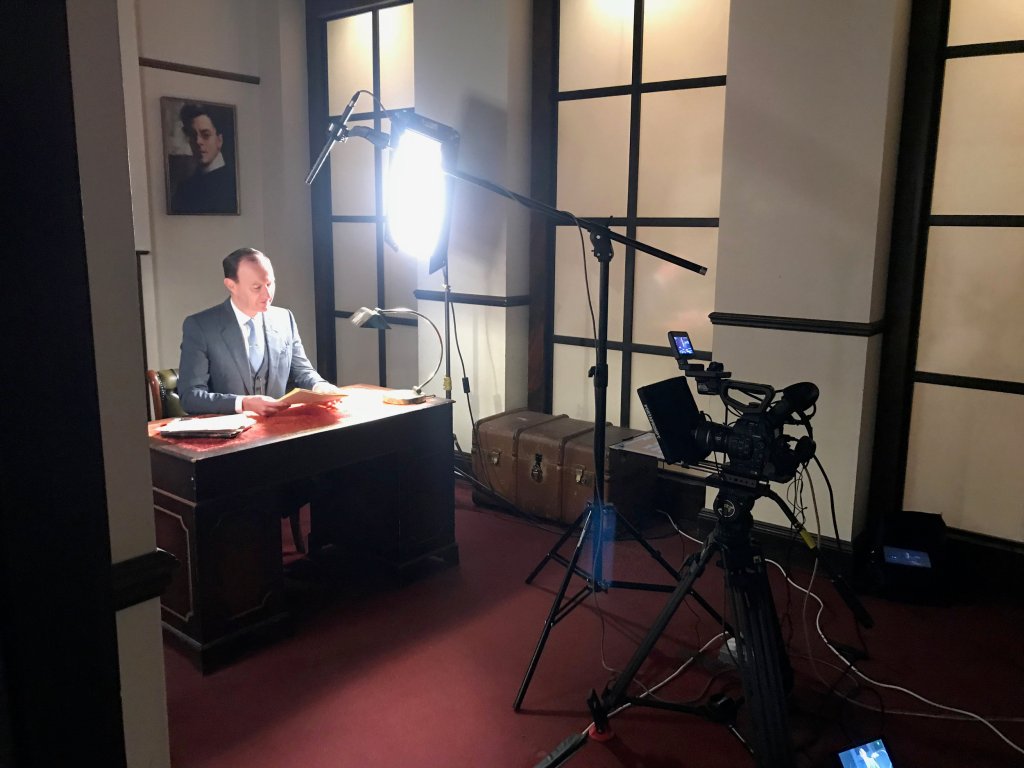 man being filmed with lights and camera sitting at a desk