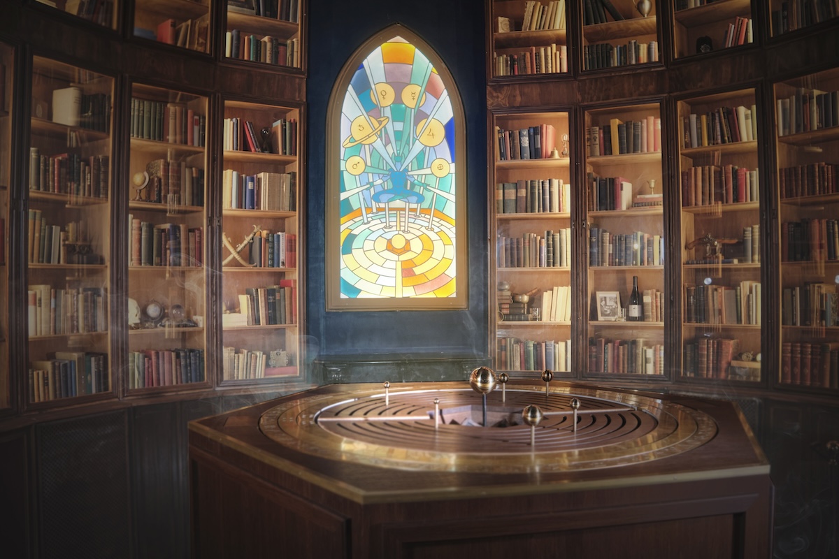 A curved wall of bookshelves that goes up to the ceiling, with a stained glass window in the middle and an orrery in front.