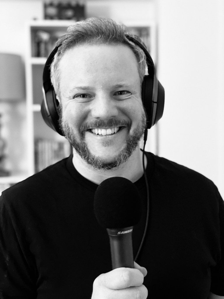 black and white photo of man smiling holding a microphone and headphones