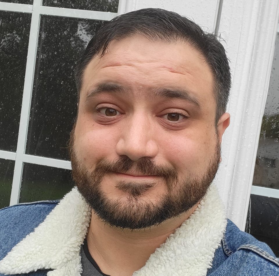 man with brown beard and short brown hair wearing a denim jacket with shearling collar