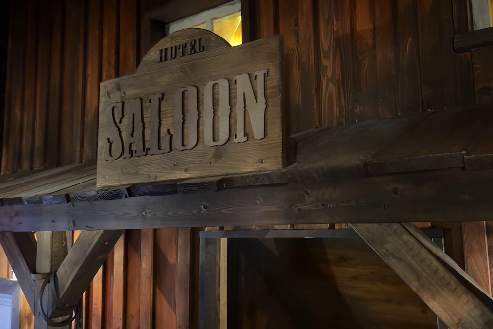 A wood sign reads "Hotel Saloon" on the exterior of an old west building.