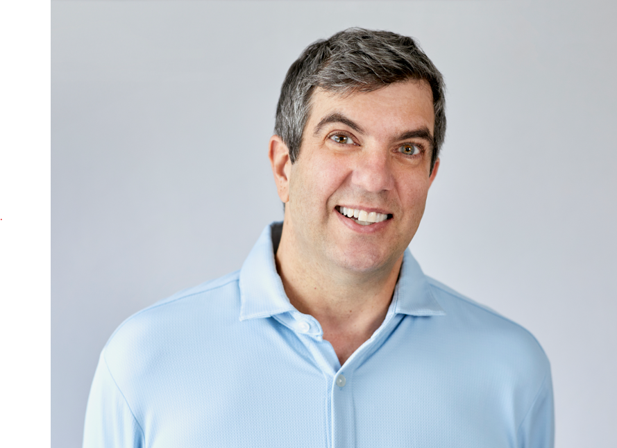 image of AJ Jacobs, caucasian man with short side parted salt and pepper hair. he has hazel eyes, clean shaven and a winsome smile. He is wearing a light blue button down shirt.