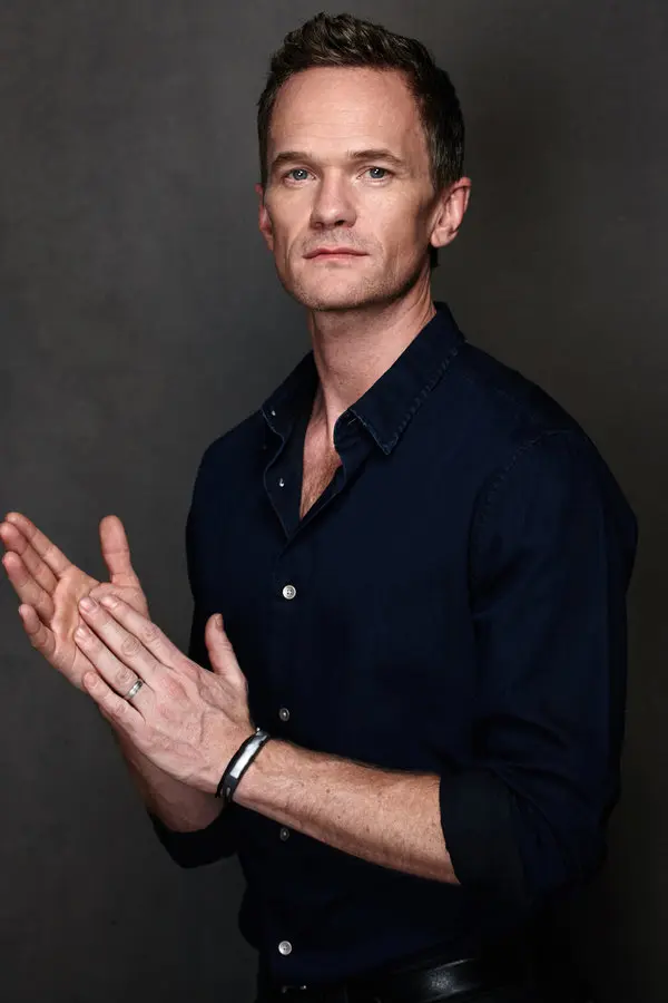 man wearing a dark blue button down shirt, neat dark blonde hair, blue eyes, clean shaven, with a contemplative look.