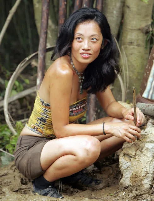 asian woman crouching in mud in the jungle, wearing a survivor buff as a tube top and wearing brown shorts